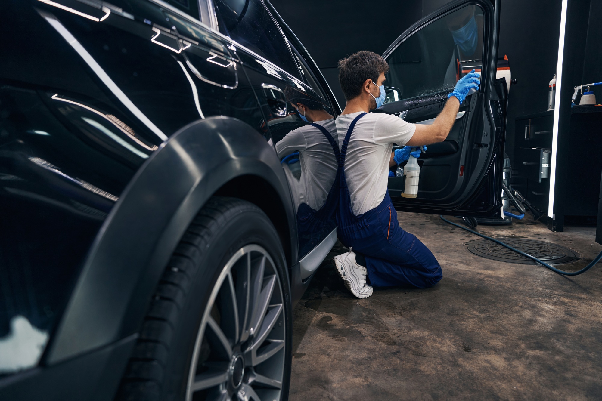 Man in repair workshop washing car window during car valeting